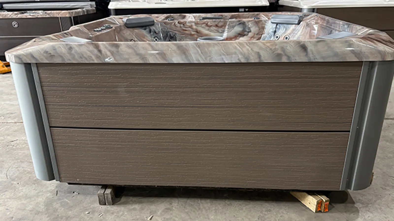 Modern rectangular hot tub with brown wooden paneling and marbled interior set on warehouse floor.