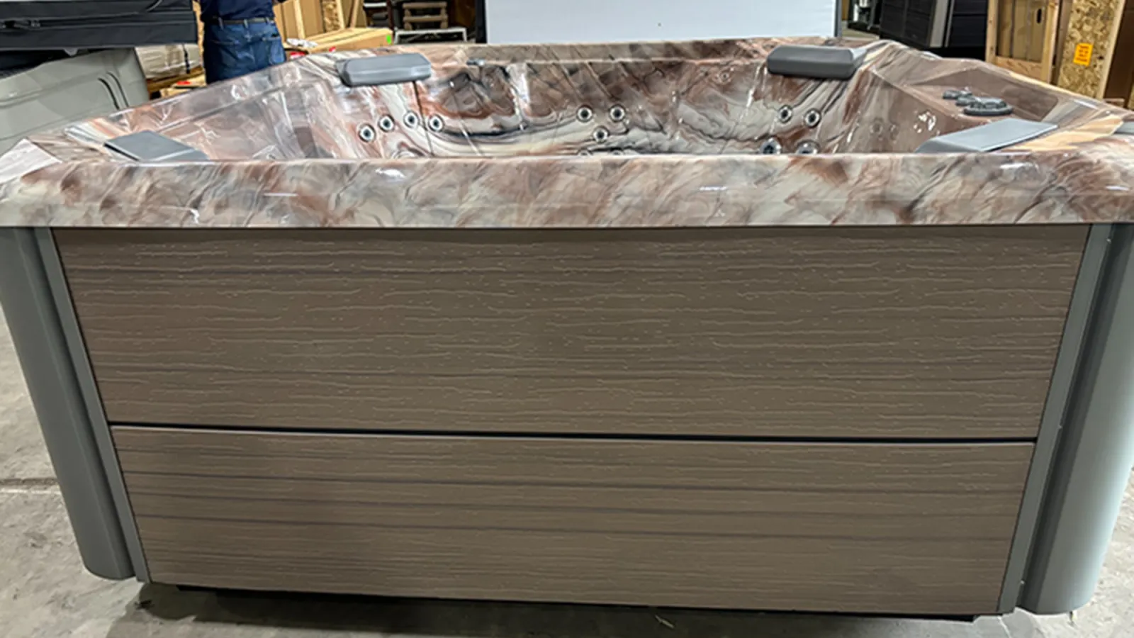 Modern hot tub with marble-patterned interior and wooden exterior panels displayed in a showroom.