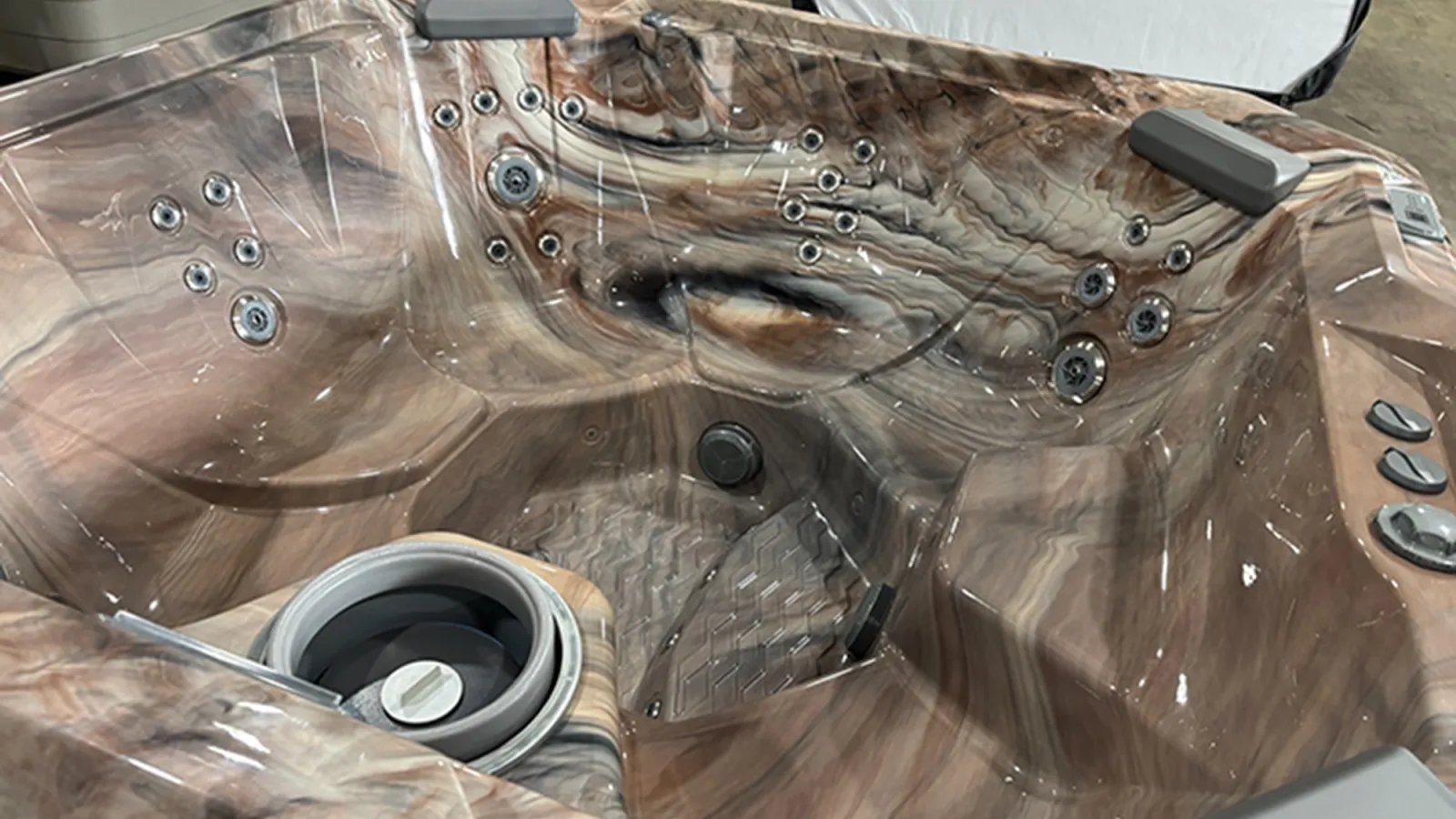 Close-up of an empty brown marbled hot tub with multiple jets, headrests, and control knobs indoors.