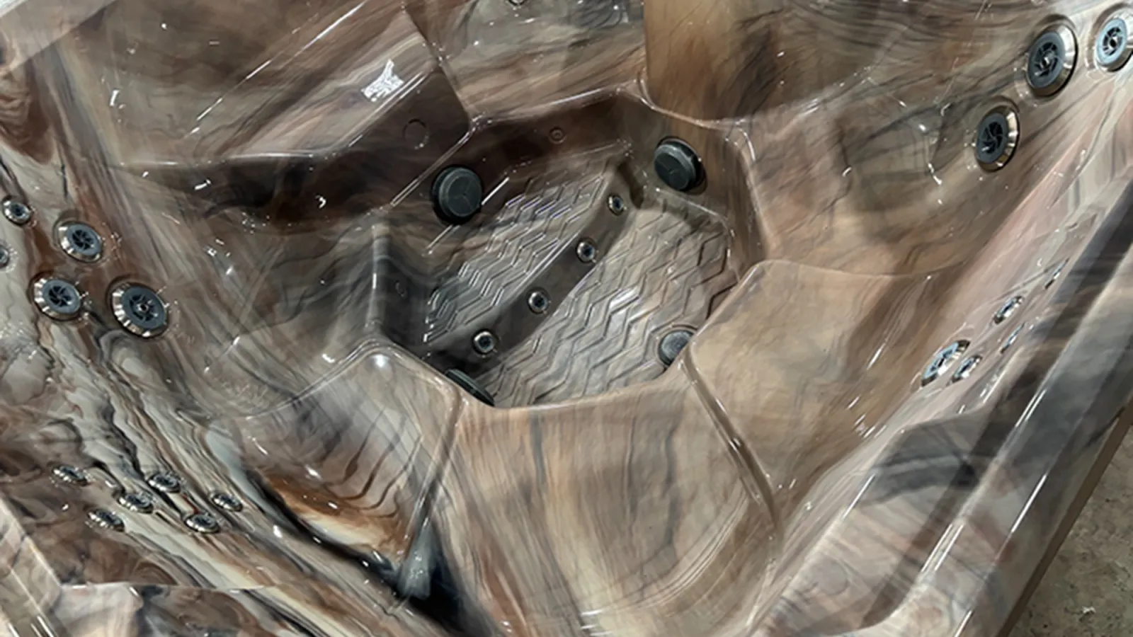 Close-up of a luxurious brown marble-patterned hot tub with multiple jet nozzles and ergonomic seating.