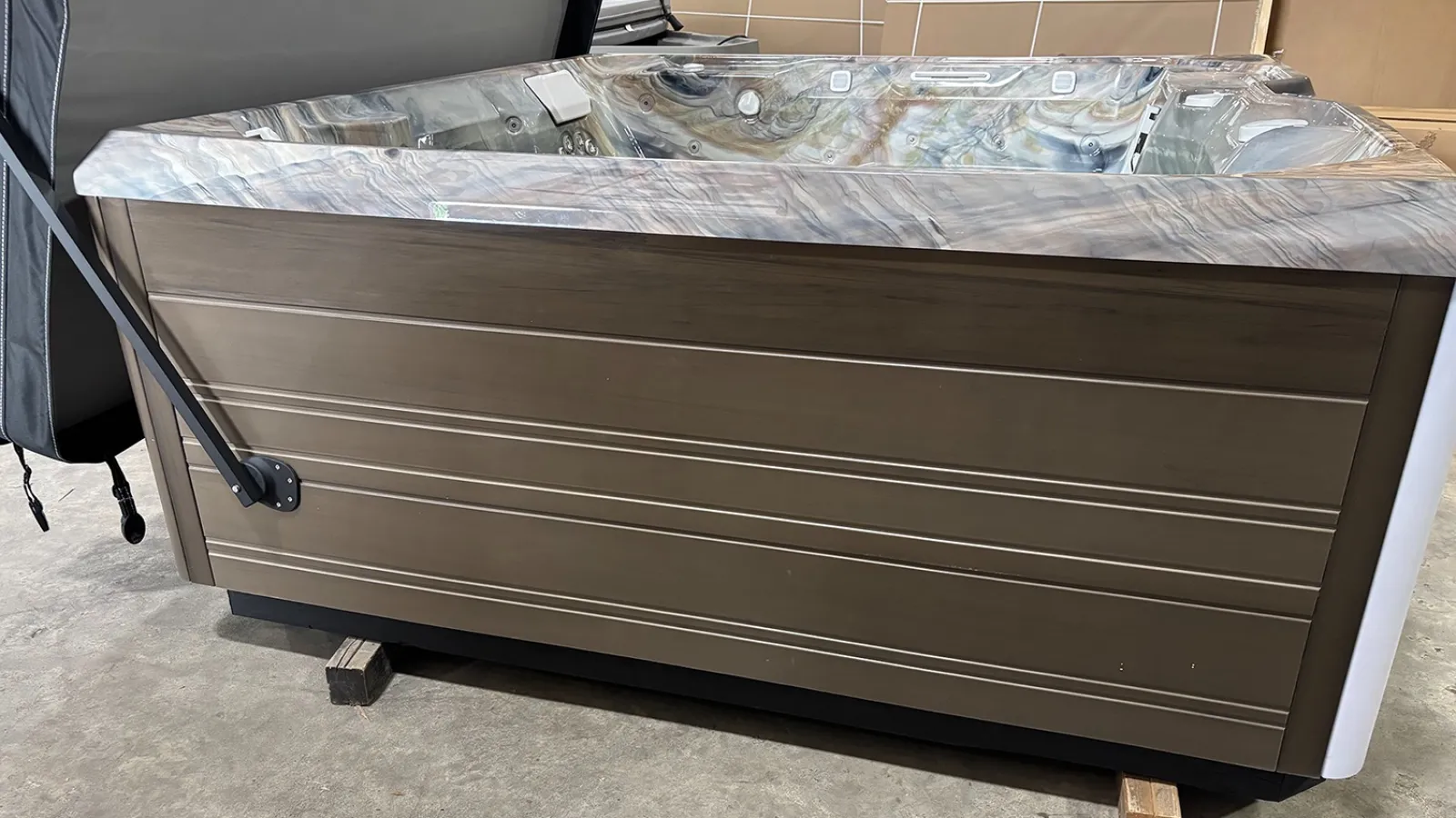 Modern brown outdoor hot tub with marble interior and lifted cover in a showroom setting.
