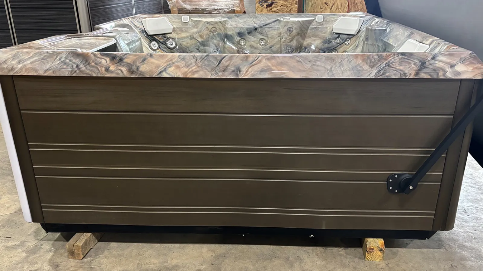 Modern rectangular hot tub with wood grain accents and multiple jets on a showroom floor.