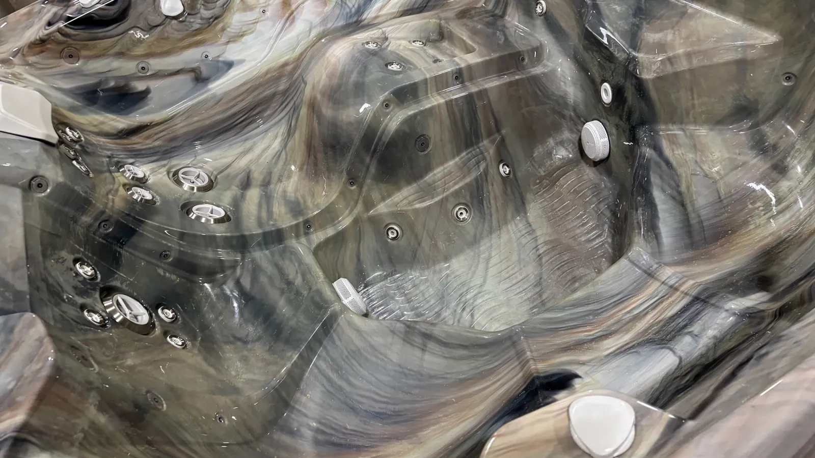 Close-up of an empty marble-patterned hot tub interior with multiple silver jets and contoured seats.