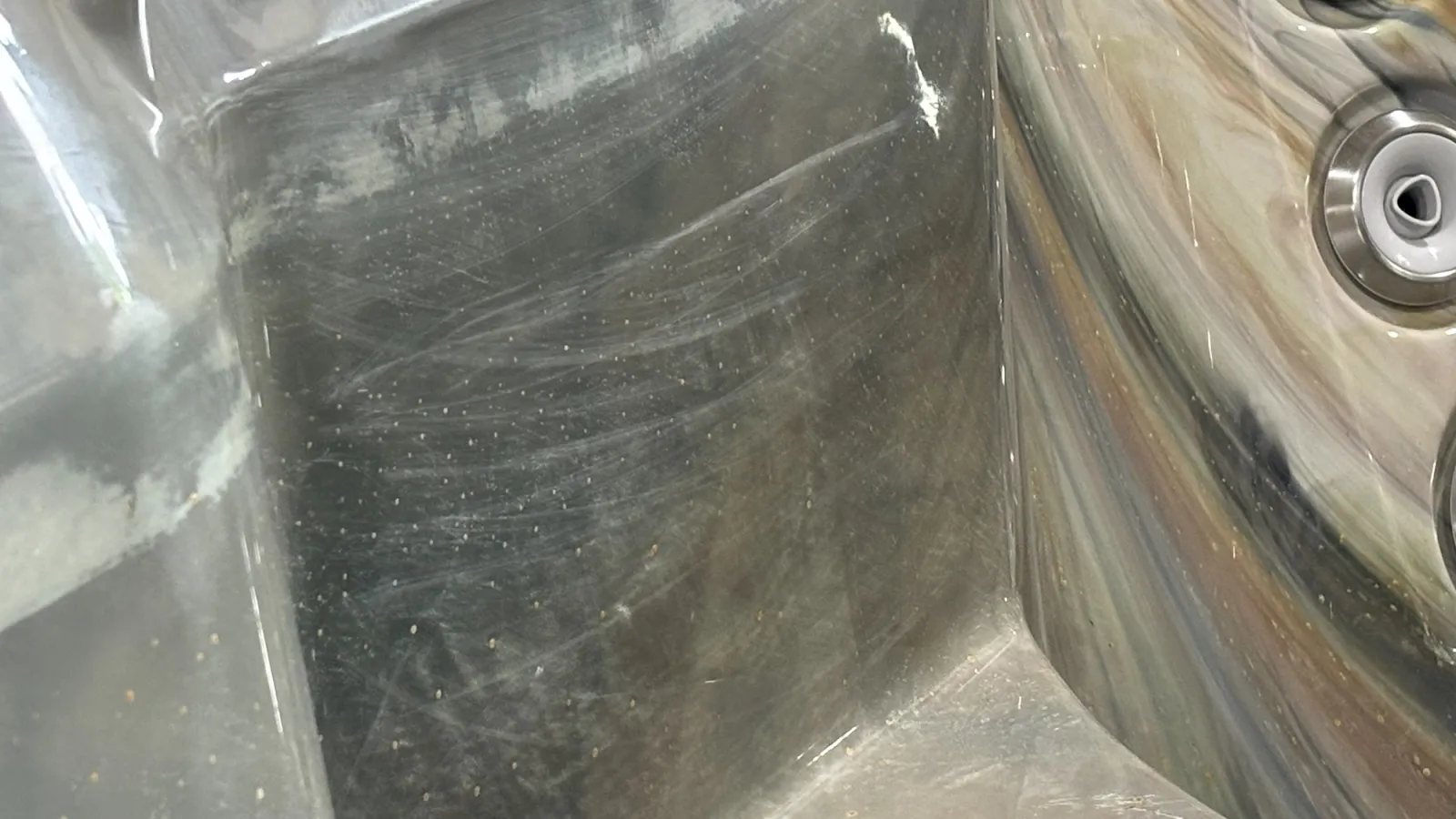 Close-up of a scratched and worn gray plastic surface with a reflective curved metallic panel and circular fixtures.