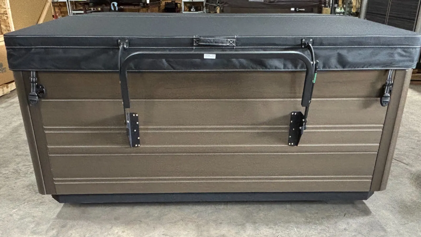 Closed brown hot tub with black cover and metal handles on concrete floor indoors.