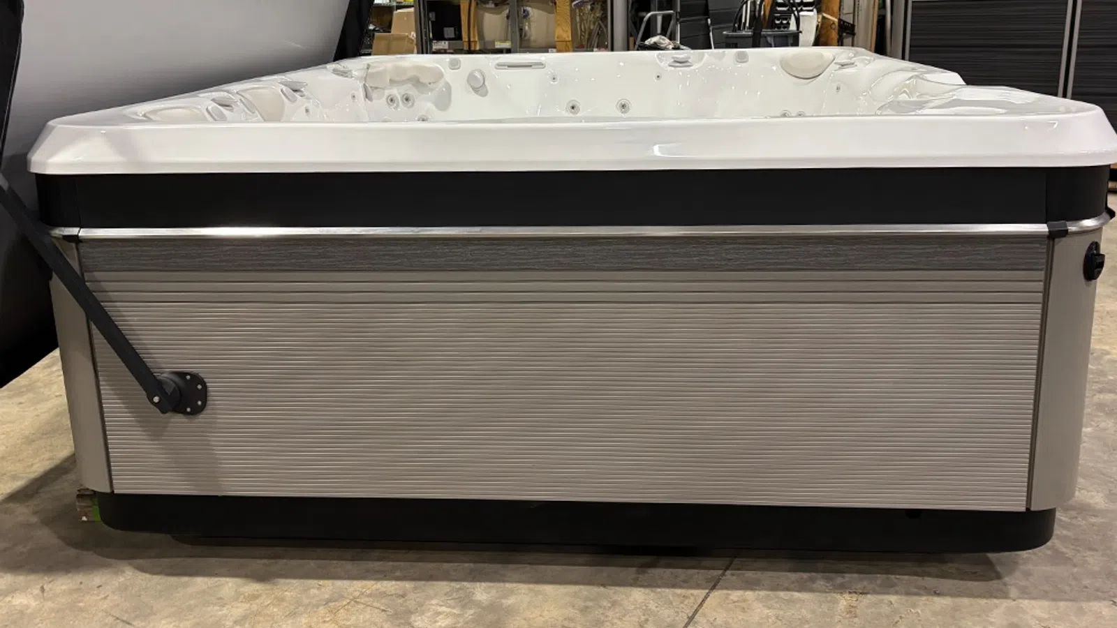 Modern rectangular hot tub with white interior and gray textured exterior panel in an indoor showroom.