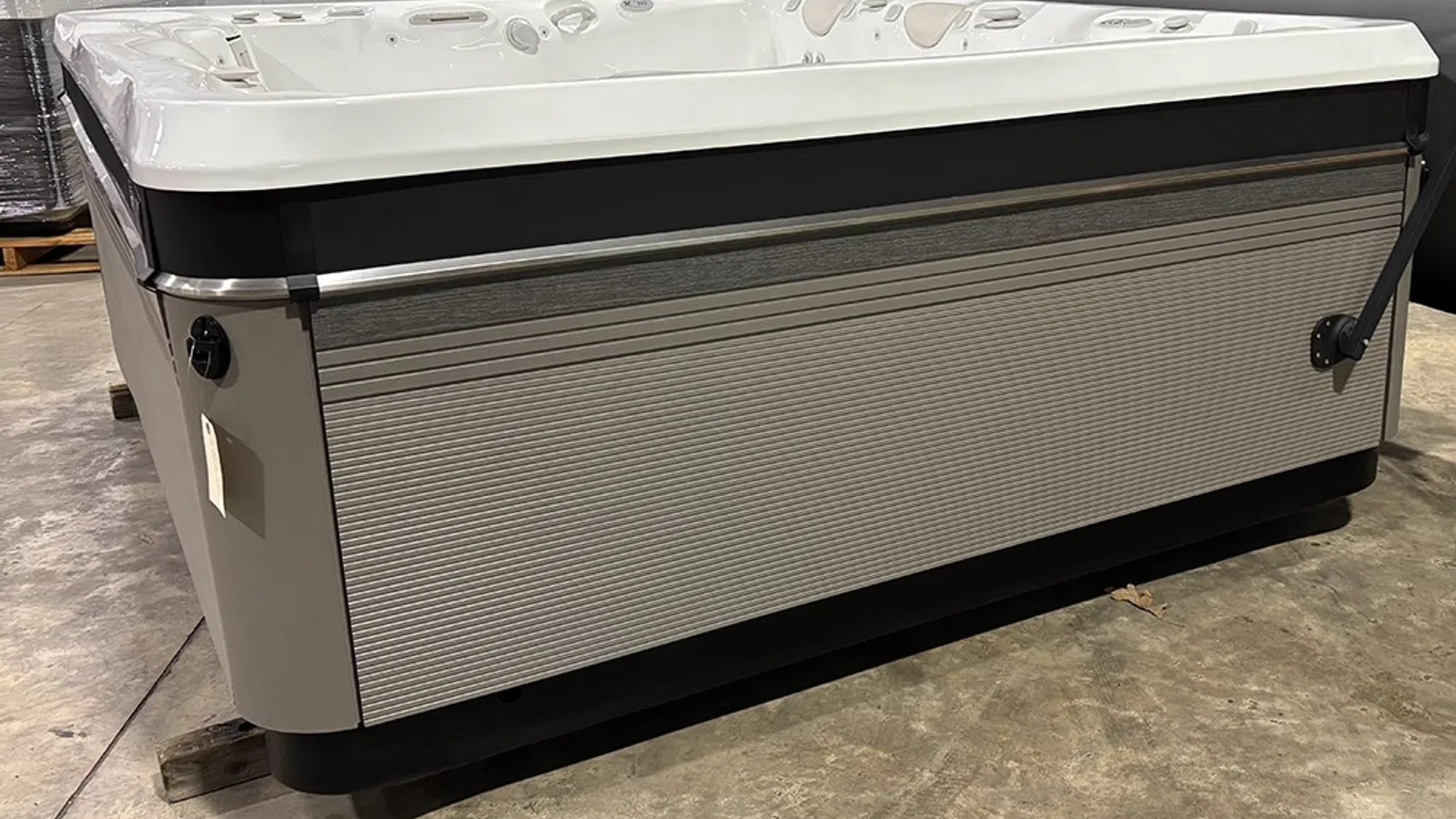 Modern rectangular spa hot tub with gray panels and white top, resting on a warehouse floor.