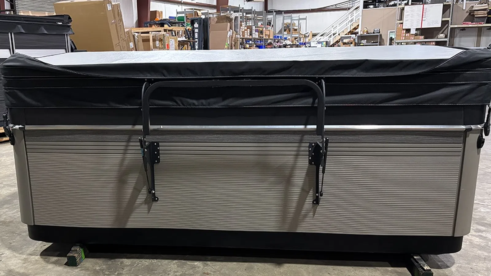 Covered hot tub with metal handrail inside a warehouse surrounded by boxes and equipment.