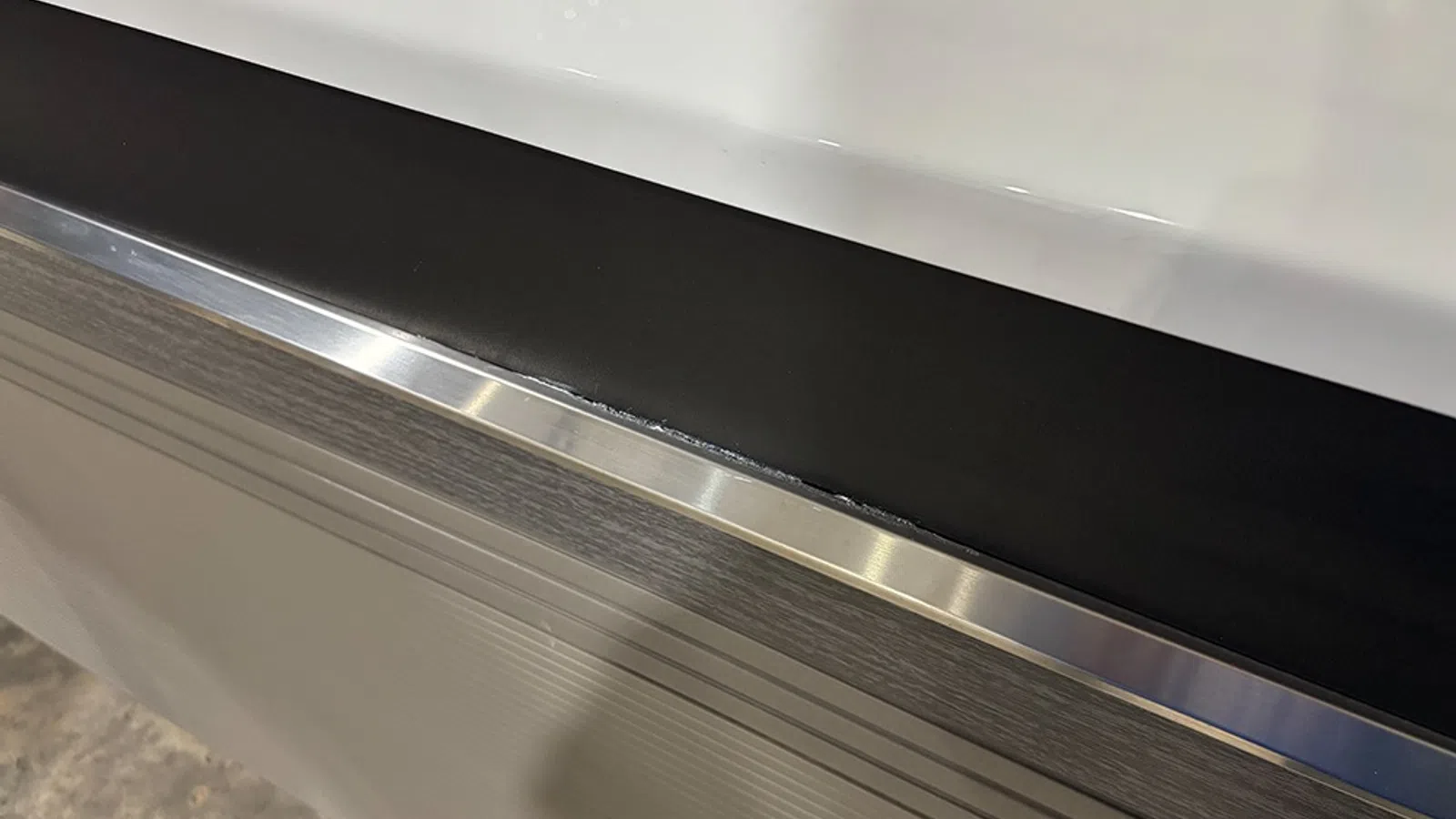 Close-up of a metal edge trim on a black and white tabletop with textured gray panel below.