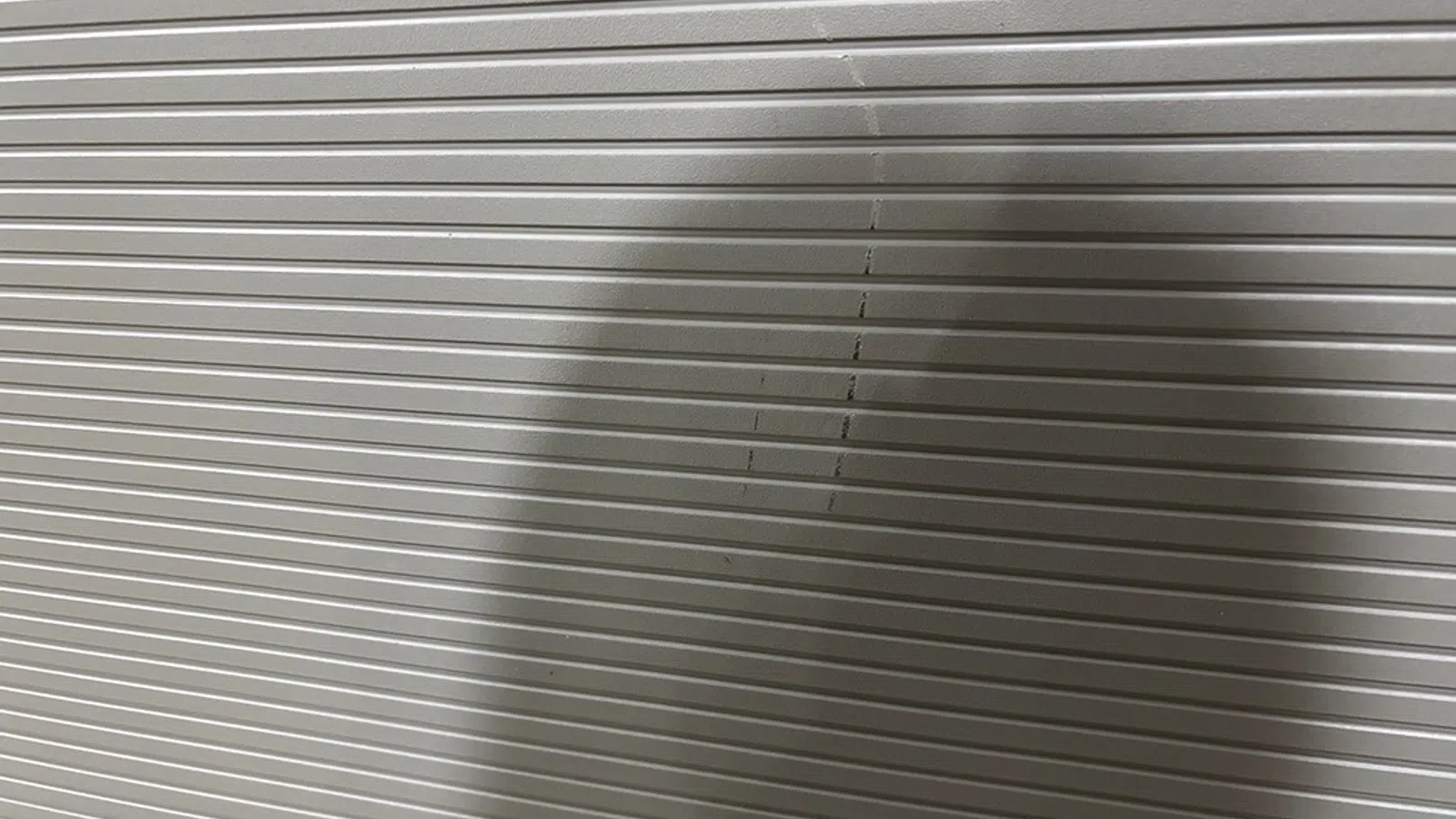 Shadow of a person cast on a metallic gray corrugated shutter with horizontal ridges.