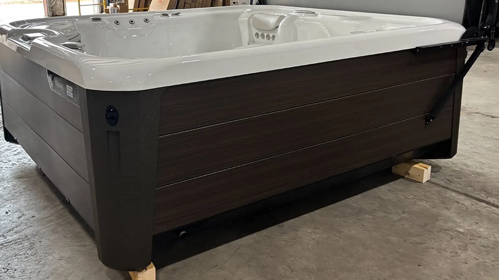 Modern brown and white outdoor hot tub with built-in jets and headrest on a concrete floor indoors.