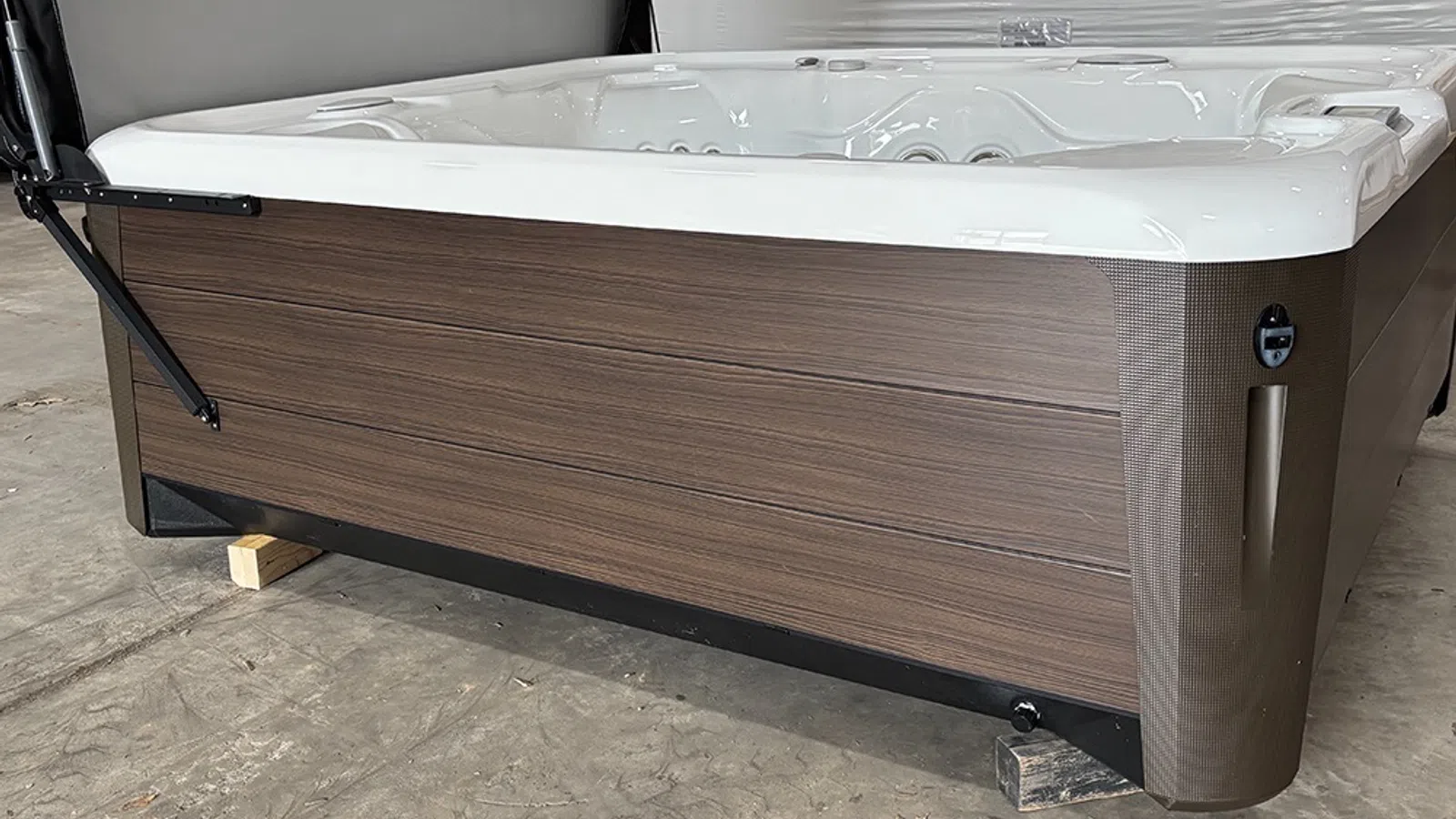 Modern hot tub with wood panel sides and white interior, set indoors on concrete floor.