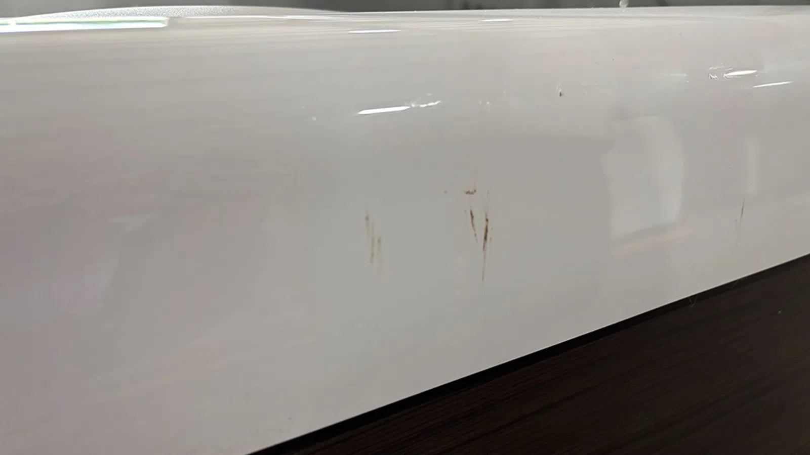 Close-up of white surface with minor scratches above a dark wood panel under soft lighting.