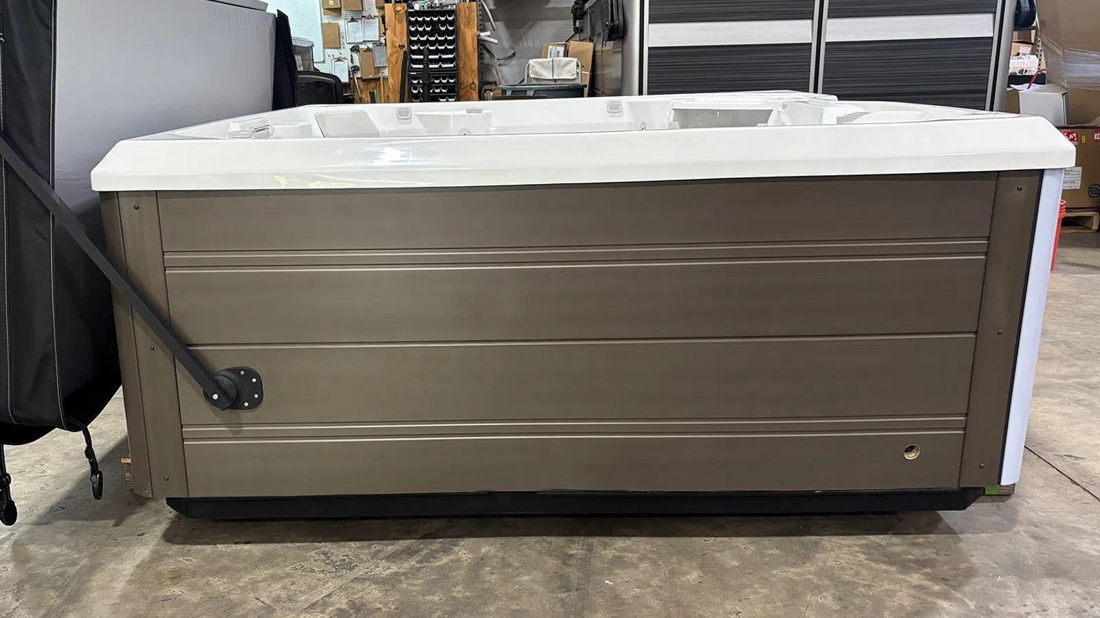 Side view of a modern rectangular hot tub with brown exterior panels in a warehouse setting.