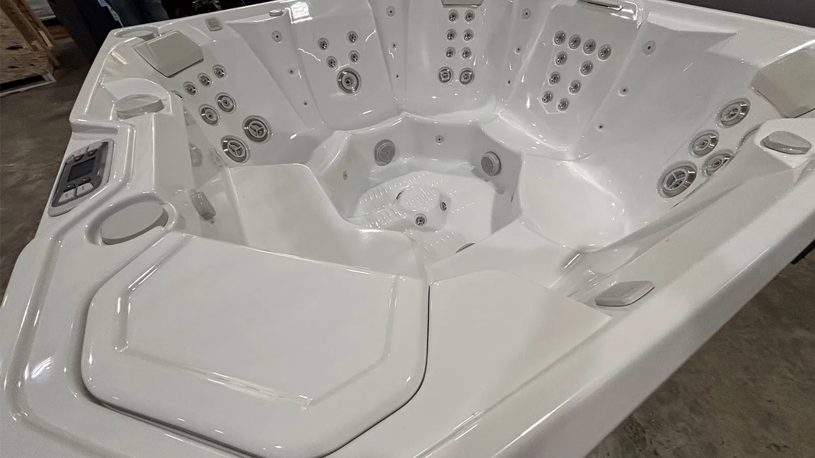 White multi-seat hot tub with numerous jets and ergonomic seating in an indoor setting.