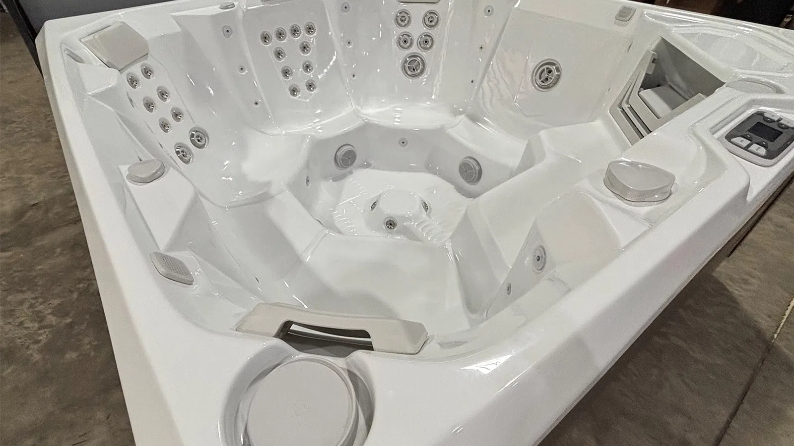 Modern white multi-seat hot tub with multiple jets and headrests in a showroom setting.