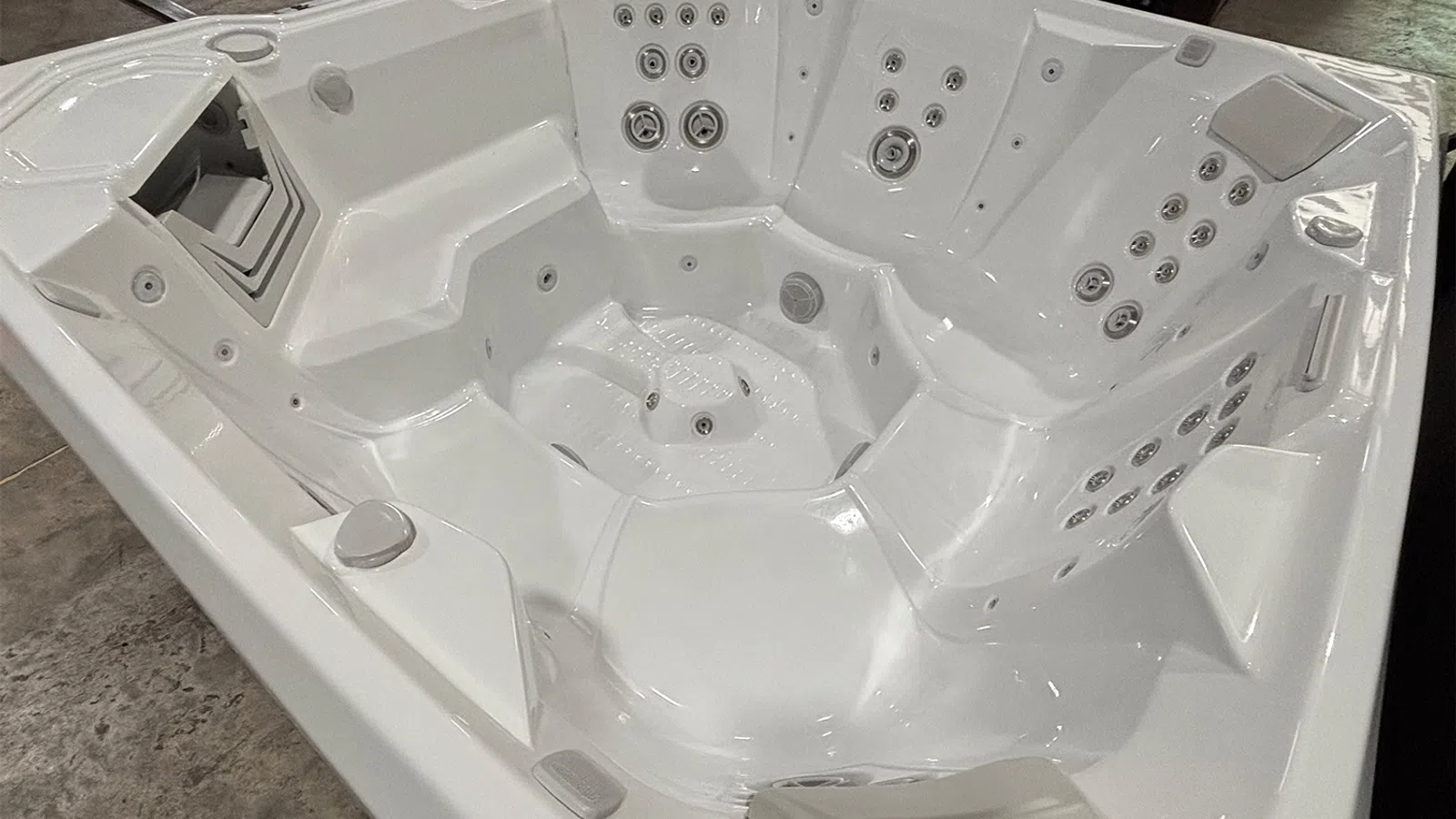 Empty white luxury hot tub with multiple jets and contoured seating in an indoor setting.