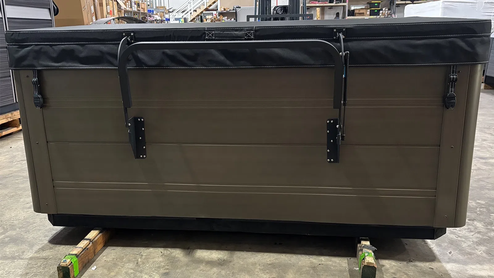 Brown and black hot tub with cover and locks on a concrete floor inside a warehouse.