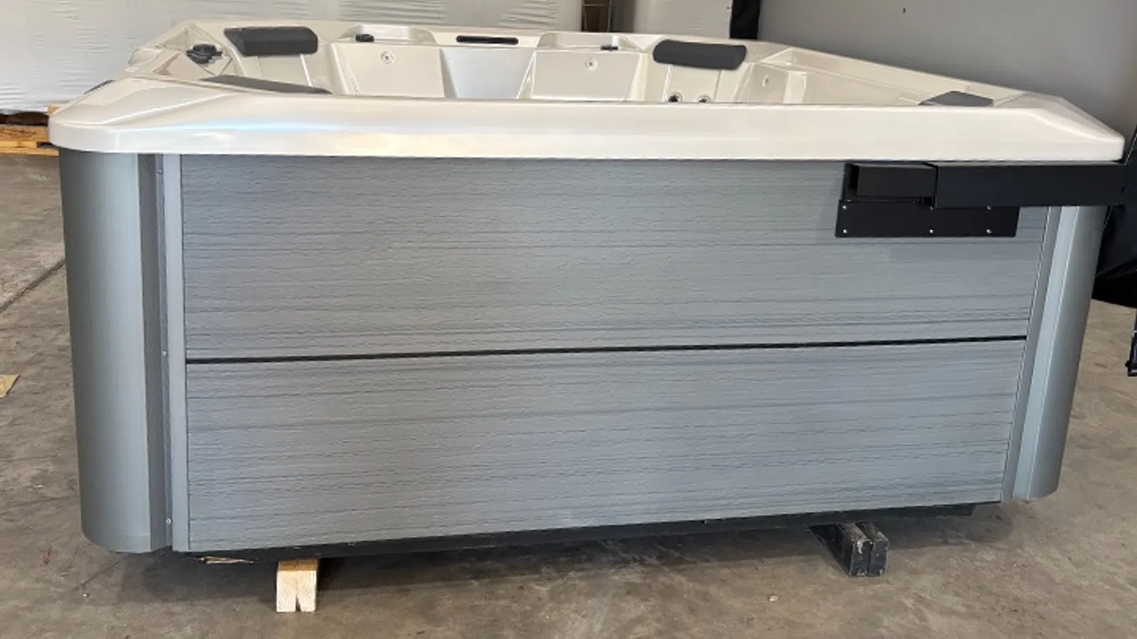 Modern gray outdoor hot tub with cup holders and headrests on a warehouse floor.