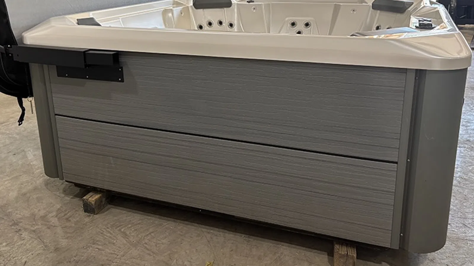 Modern gray outdoor hot tub with white interior seating and jets on a concrete floor indoors.