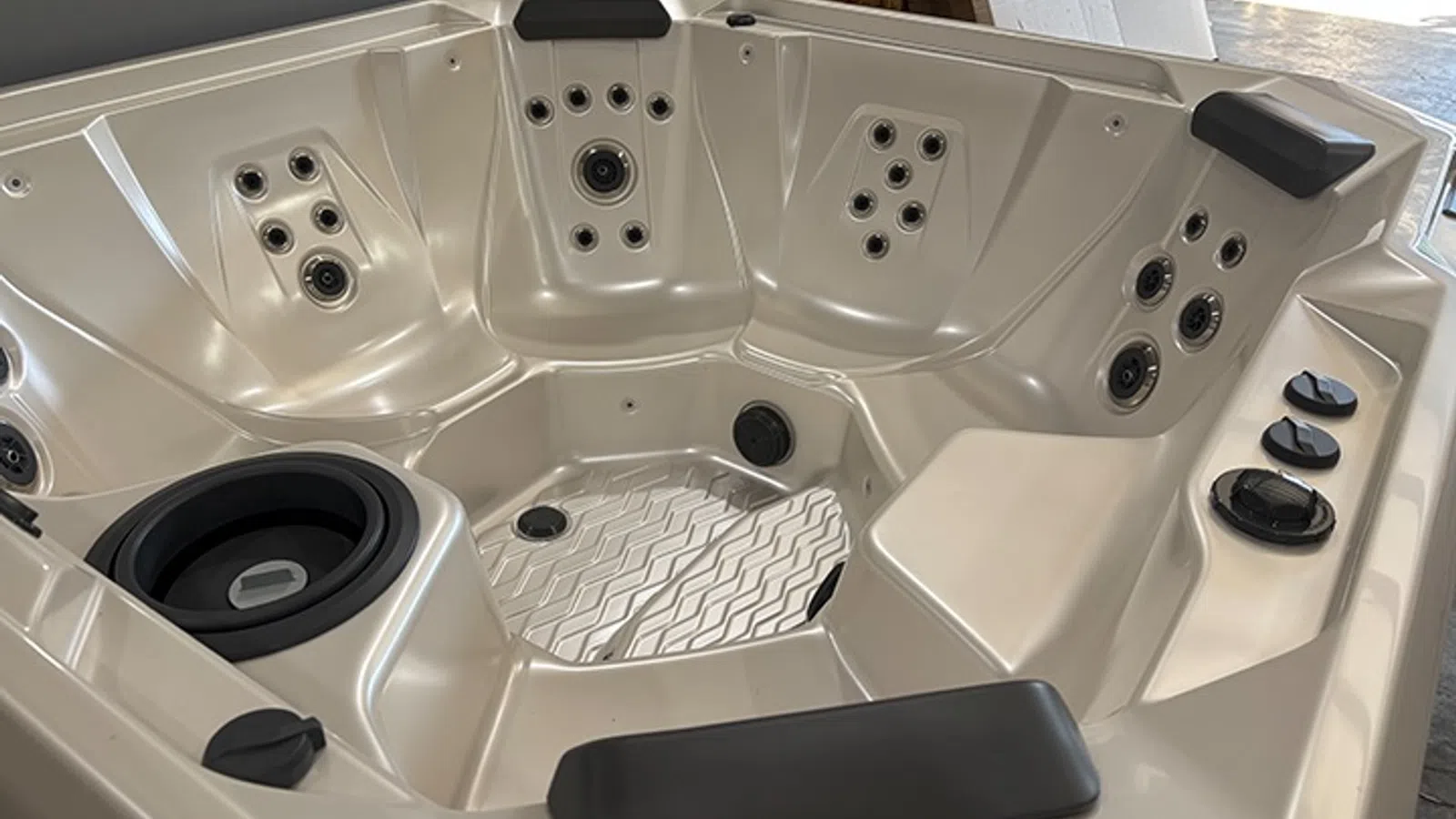 Empty beige hot tub with multiple jet nozzles, black headrests, and textured seating area indoors.