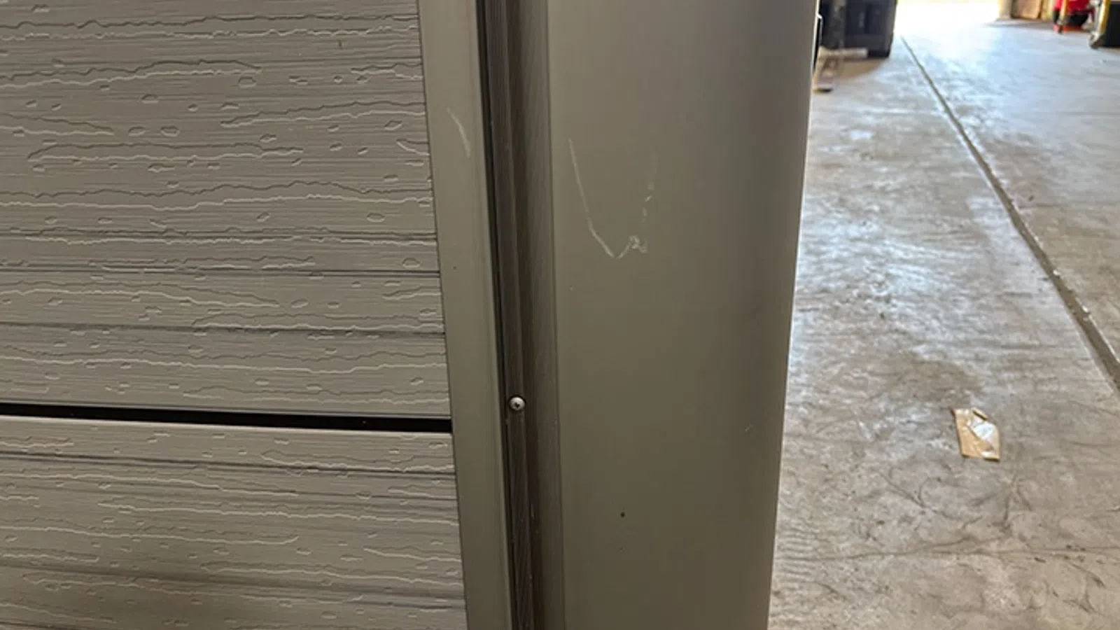 Close-up of a corner joint between a beige garage door and a gray vertical metal frame in a warehouse setting.