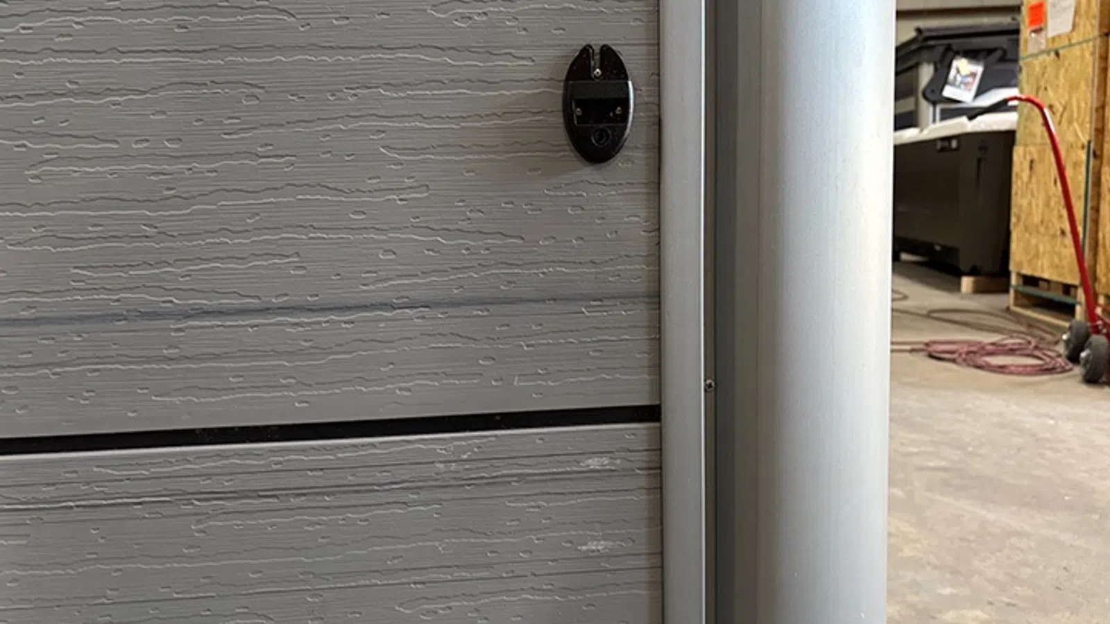 Close-up of a gray textured garage door panel and metal vertical frame in a workshop setting.