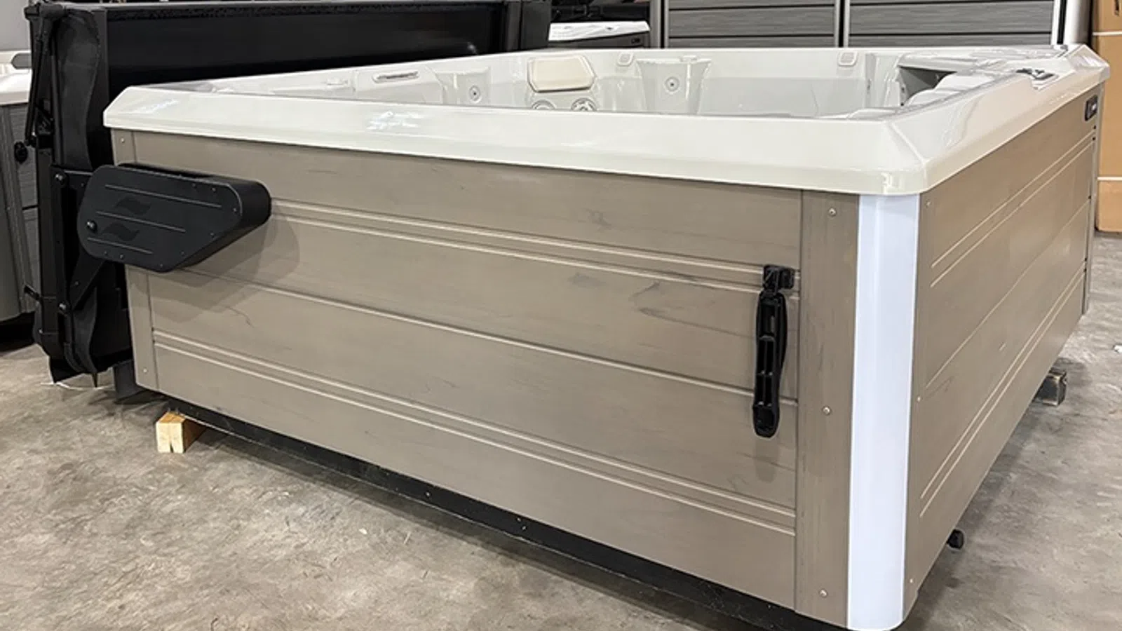 Modern beige and white rectangular hot tub with black handles and cover lifter set on concrete floor indoors.