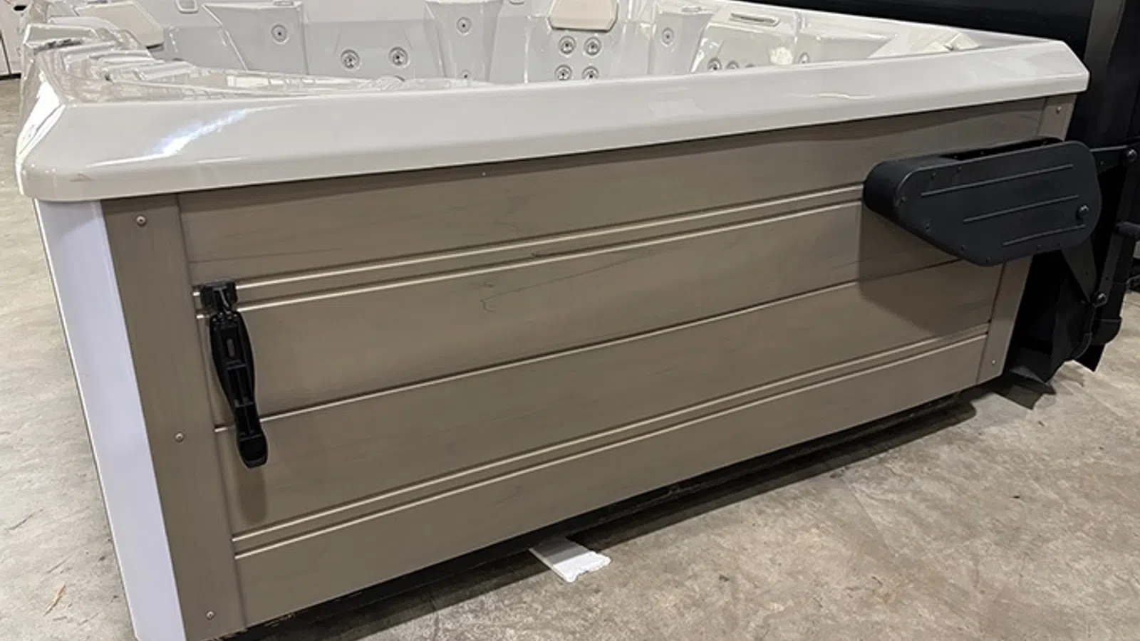 Side view of a beige and white outdoor hot tub with built-in jets and attached cover lifter on a concrete floor