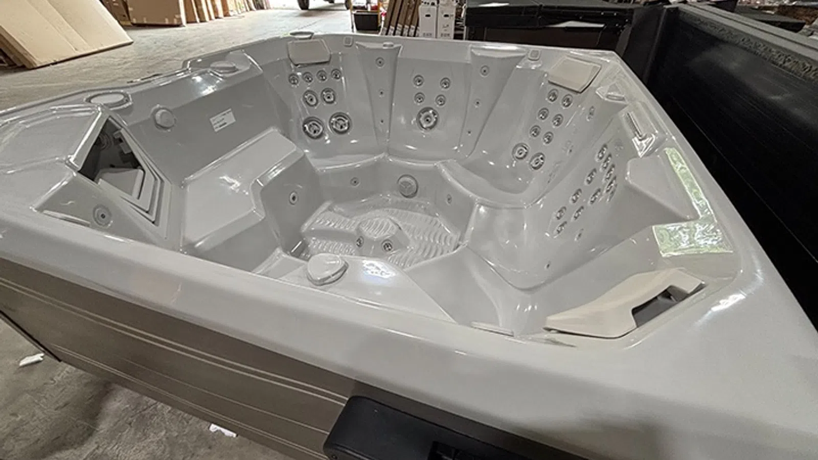 Empty white luxury hot tub with multiple seating areas and jets in a warehouse setting