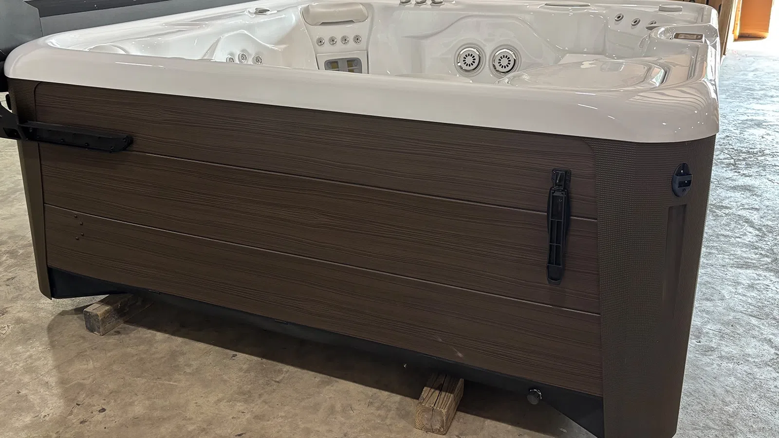 Modern rectangular hot tub with brown wood-like panels and white interior jets on a concrete floor.