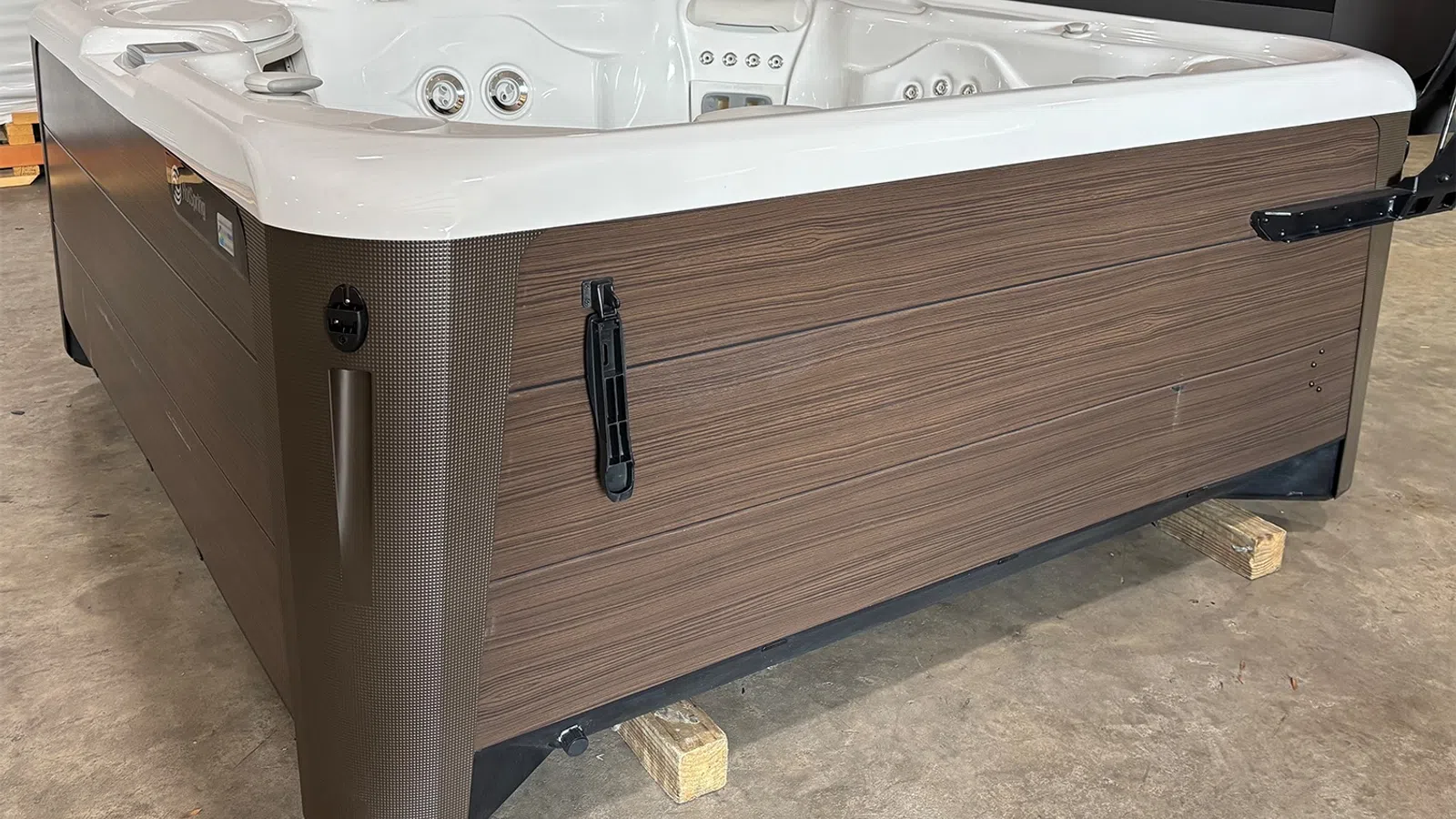 Modern rectangular hot tub with wood panel exterior and white interior jets set on wooden blocks indoors.