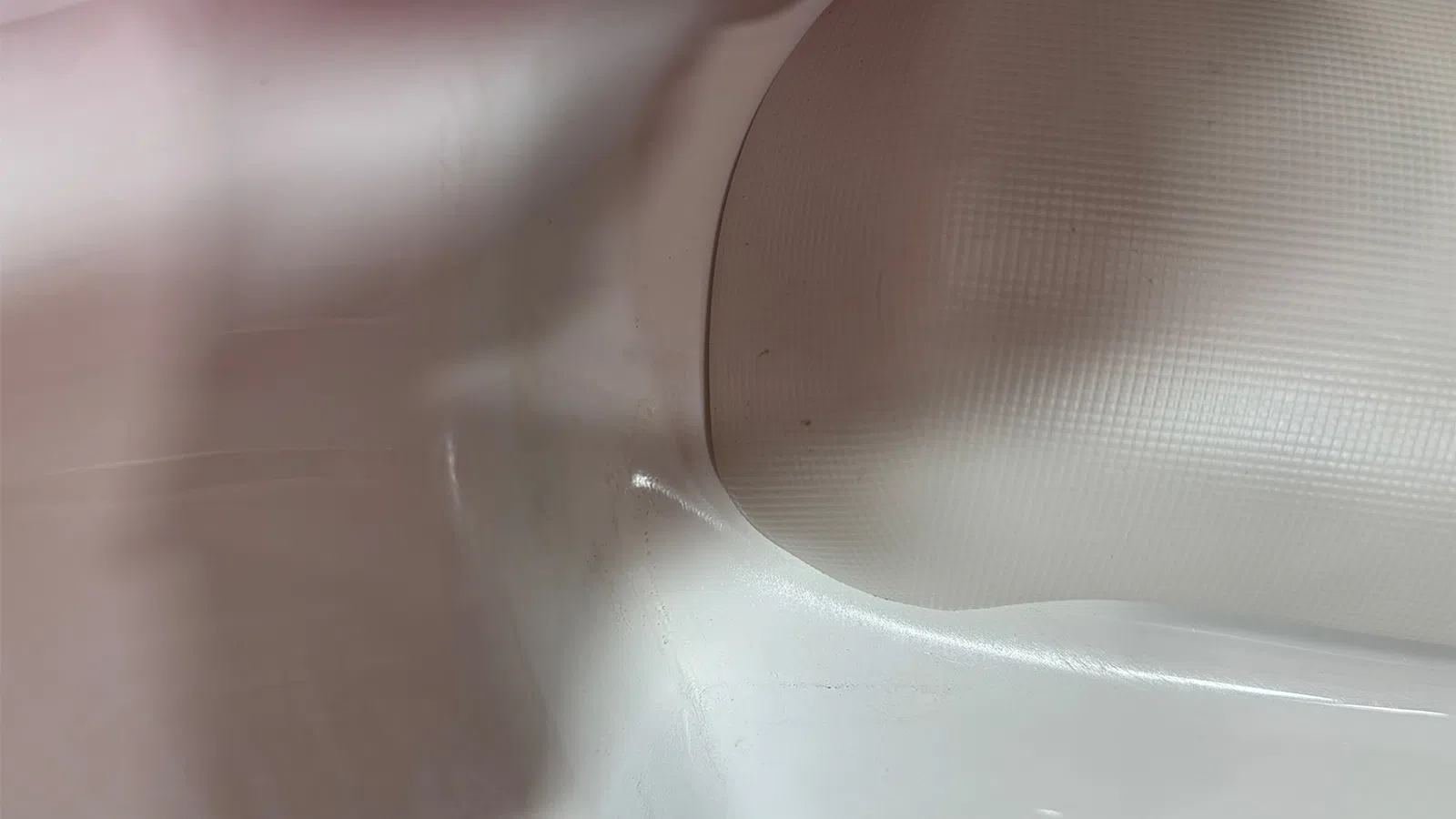Close-up of a white plastic surface with a textured curved edge and smooth glossy area under soft lighting.