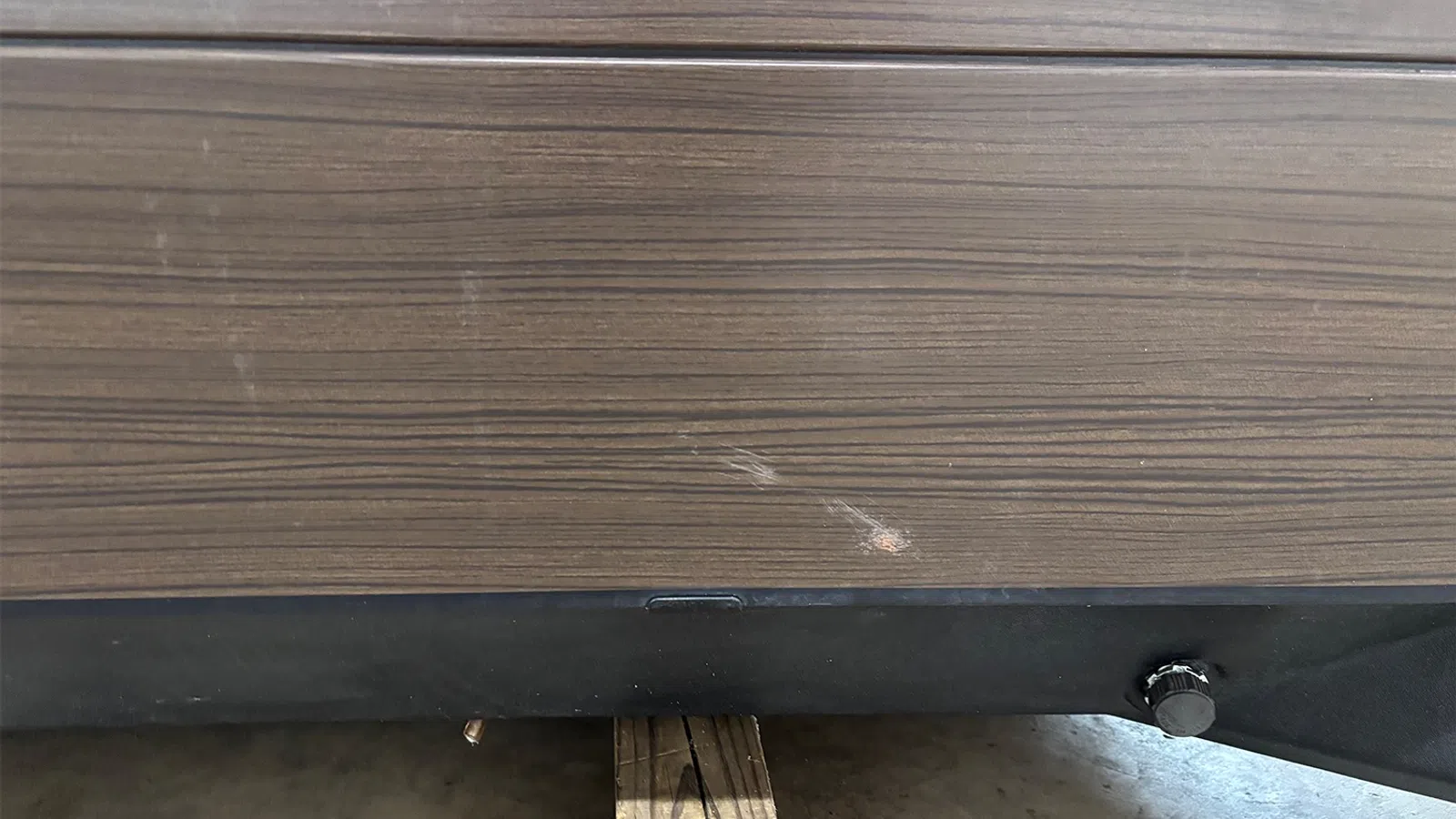Close-up of wood-textured surface with black base and wooden support underneath on concrete floor.