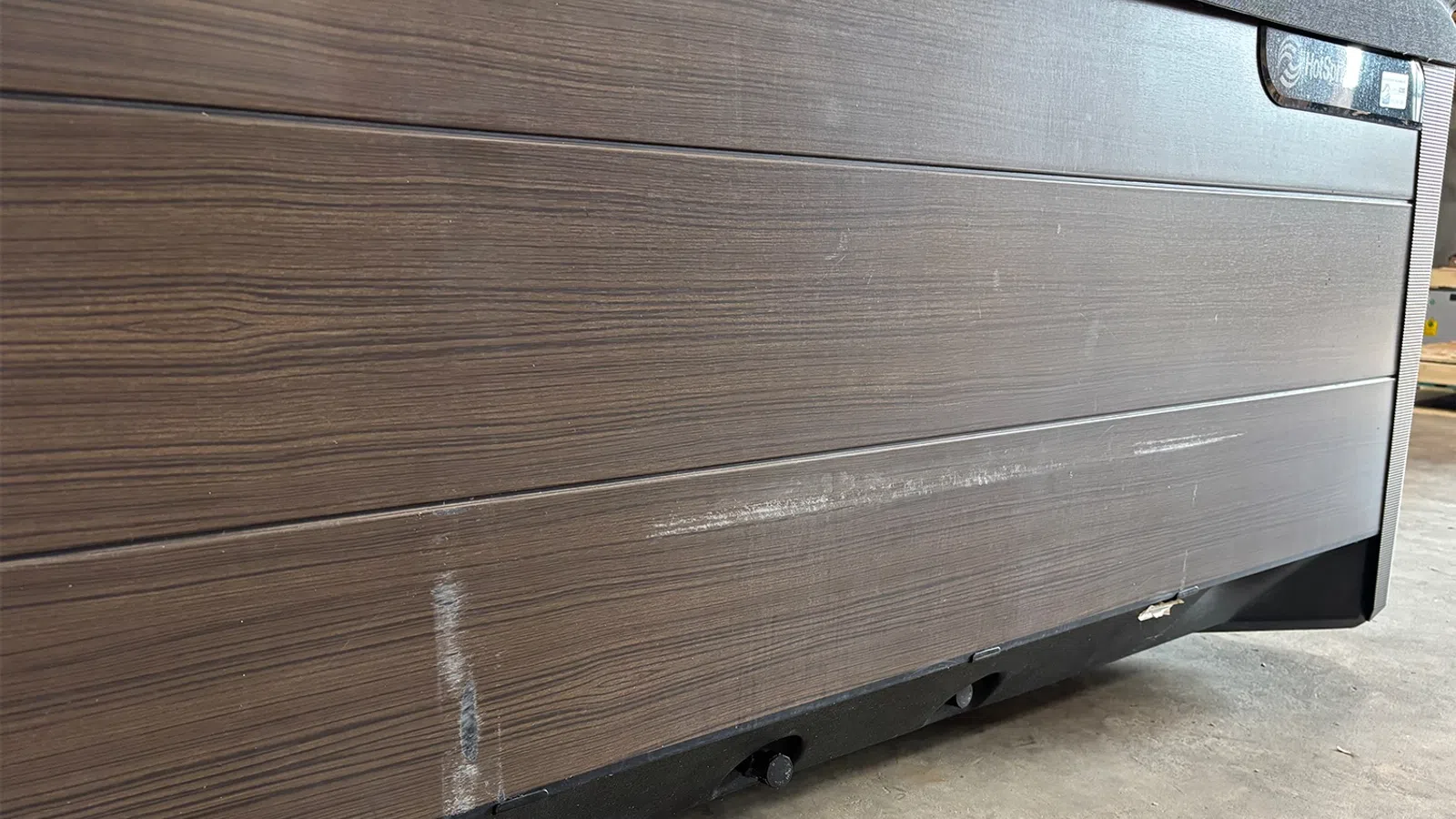 Close-up of a scratched wooden panel with a black base on a concrete floor indoors.
