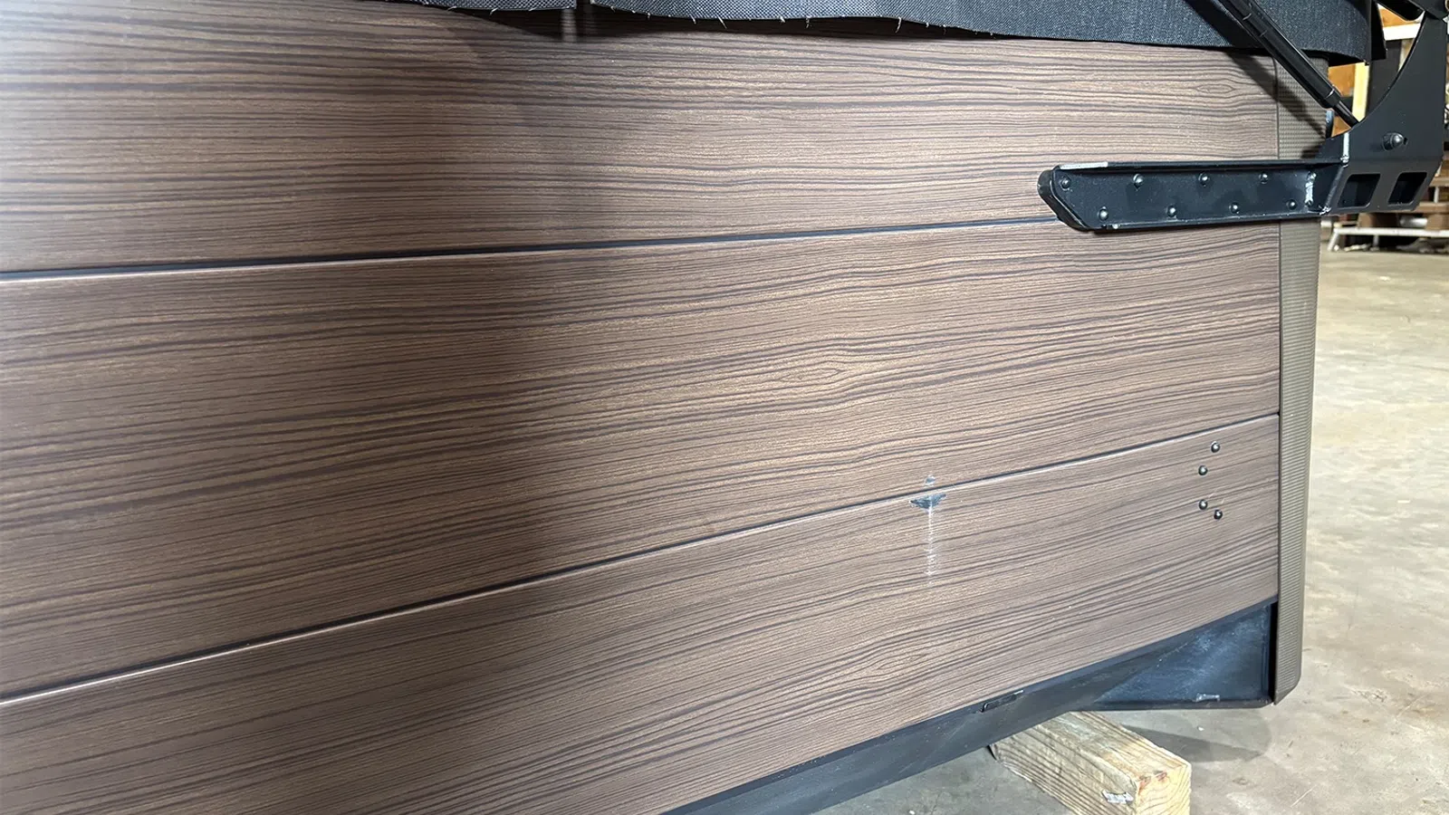 Close-up of brown wood-textured panel with metal brackets and support block in a workshop setting.