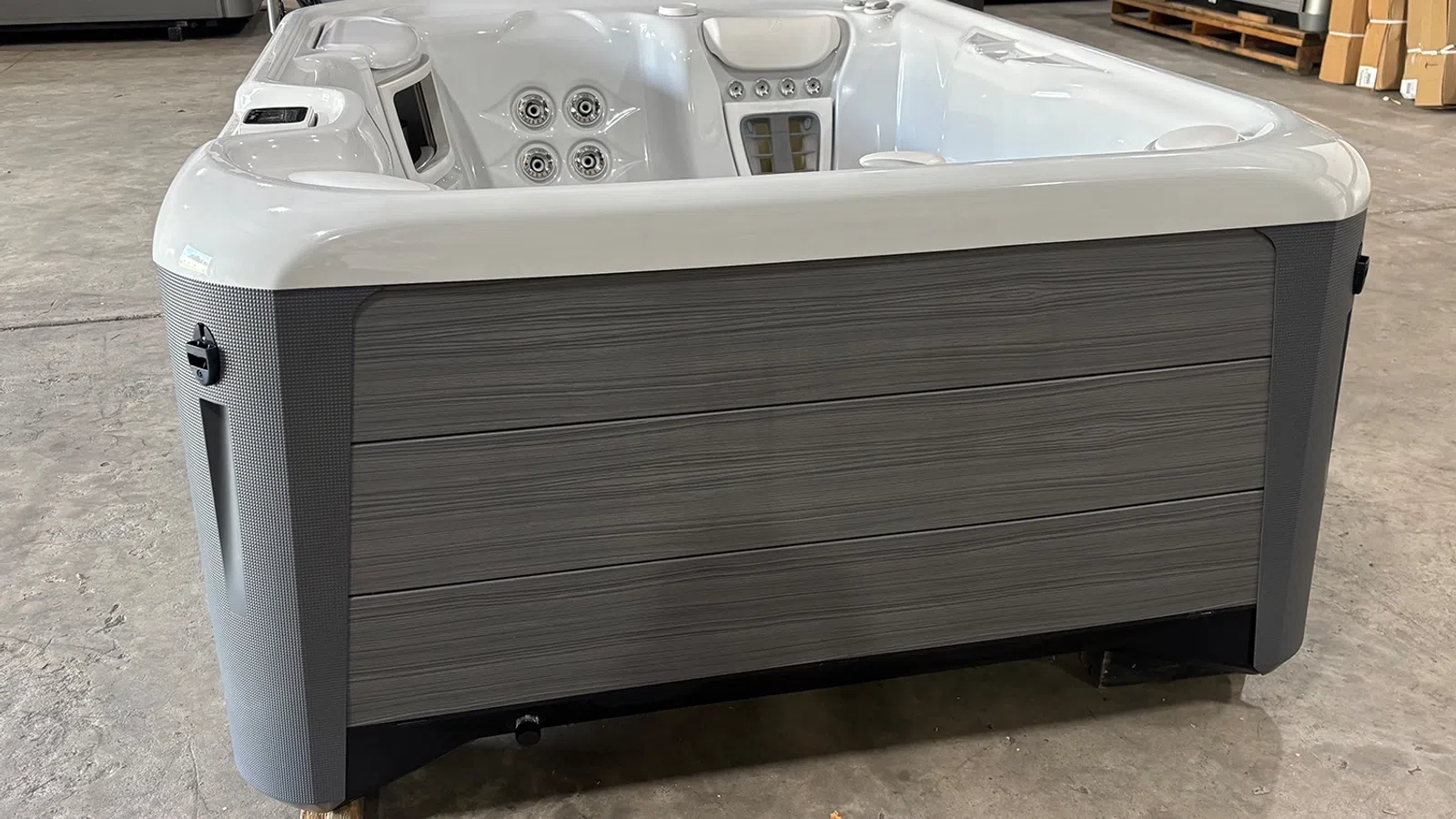 Modern outdoor hot tub with gray wood paneling and white interior featuring seating and jets.