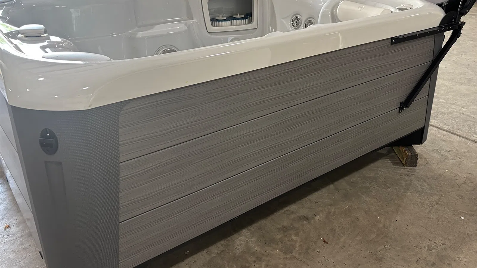 Gray and white modern hot tub with wood-look paneling on a concrete floor in an indoor setting.