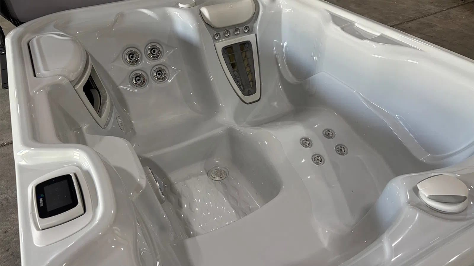 Empty white modern hot tub with multiple jets, built-in control panel, and ergonomic seating indoors.