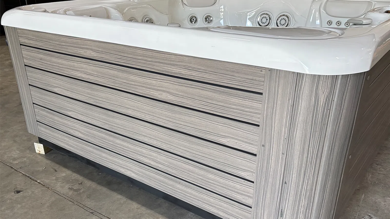 Modern outdoor hot tub with white interior and wood panel exterior on concrete floor indoors