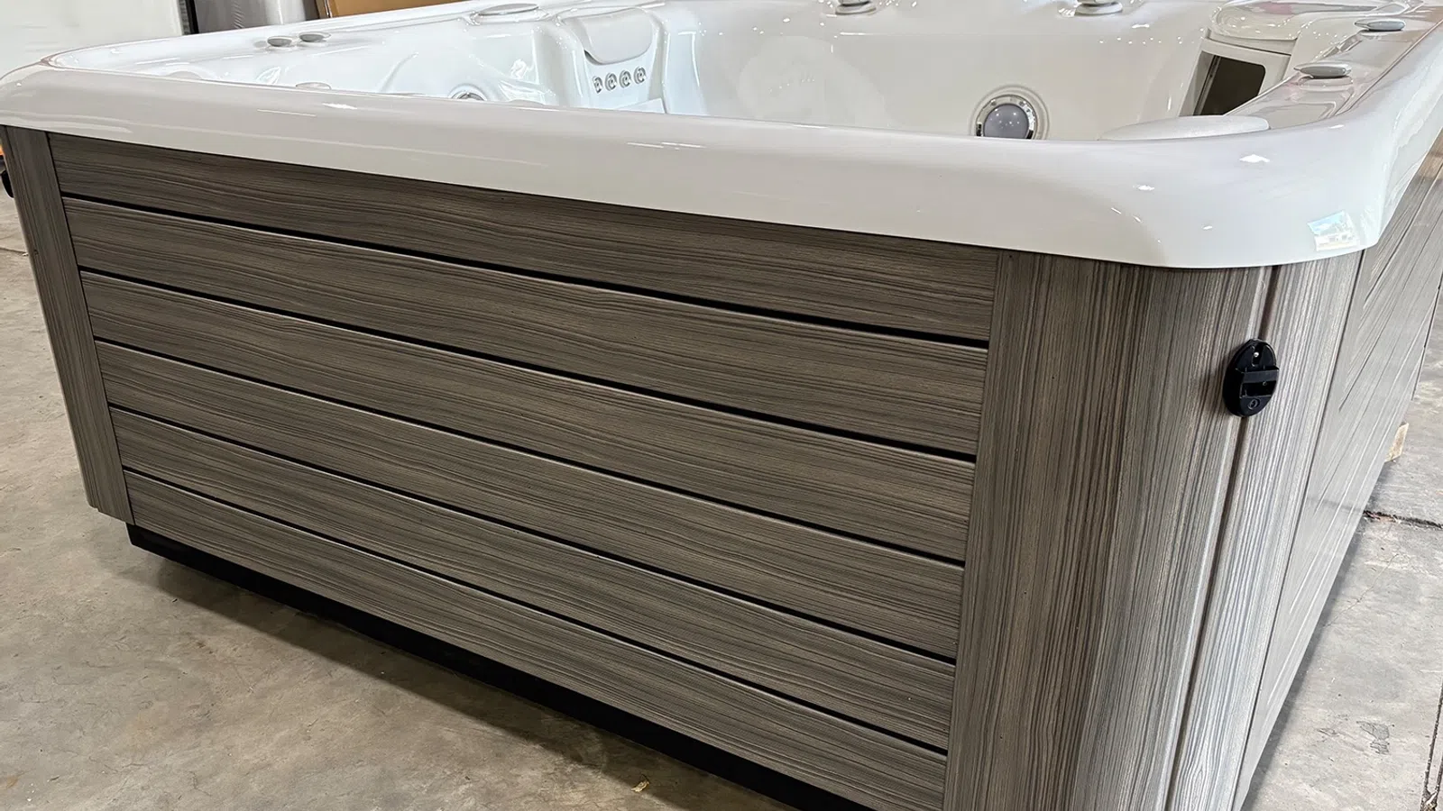 Modern outdoor hot tub with wood-textured panels and white interior shell on a concrete floor.