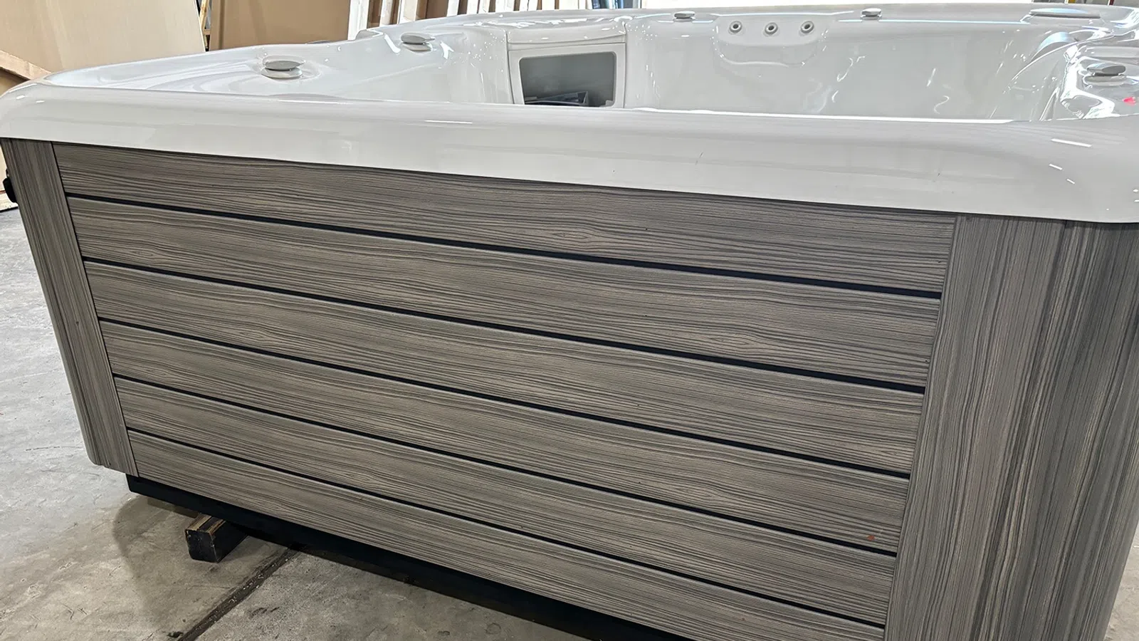 Modern hot tub with wood-like panel exterior and white acrylic interior sitting on concrete floor.