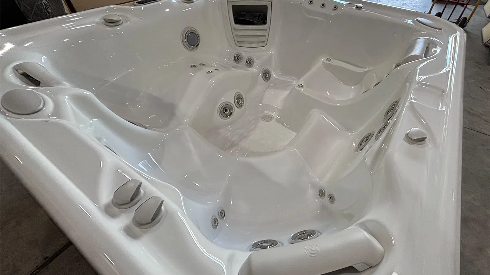 Close-up of a clean white hot tub with multiple jets, ergonomic seating, and control knobs inside a garage.