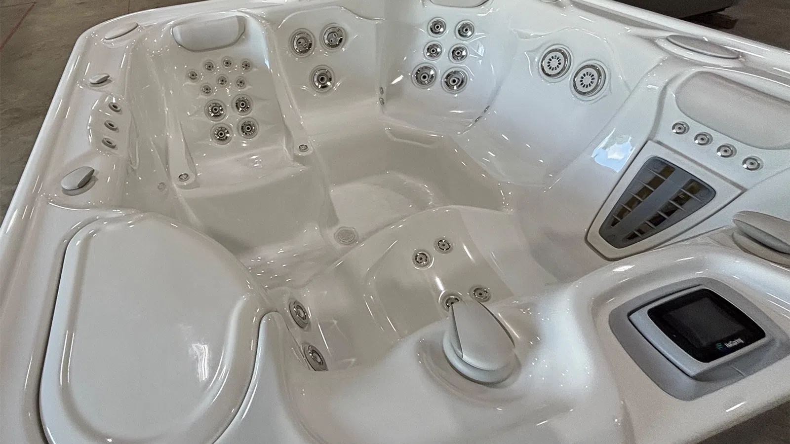 White modern hot tub interior with multiple jets, ergonomic seats, and a digital control panel visible.