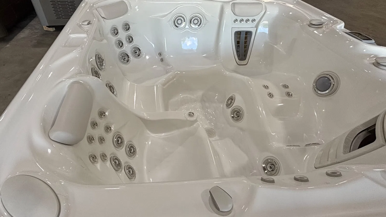 White luxury hot tub with multiple jet nozzles and ergonomic seats in an indoor setting.