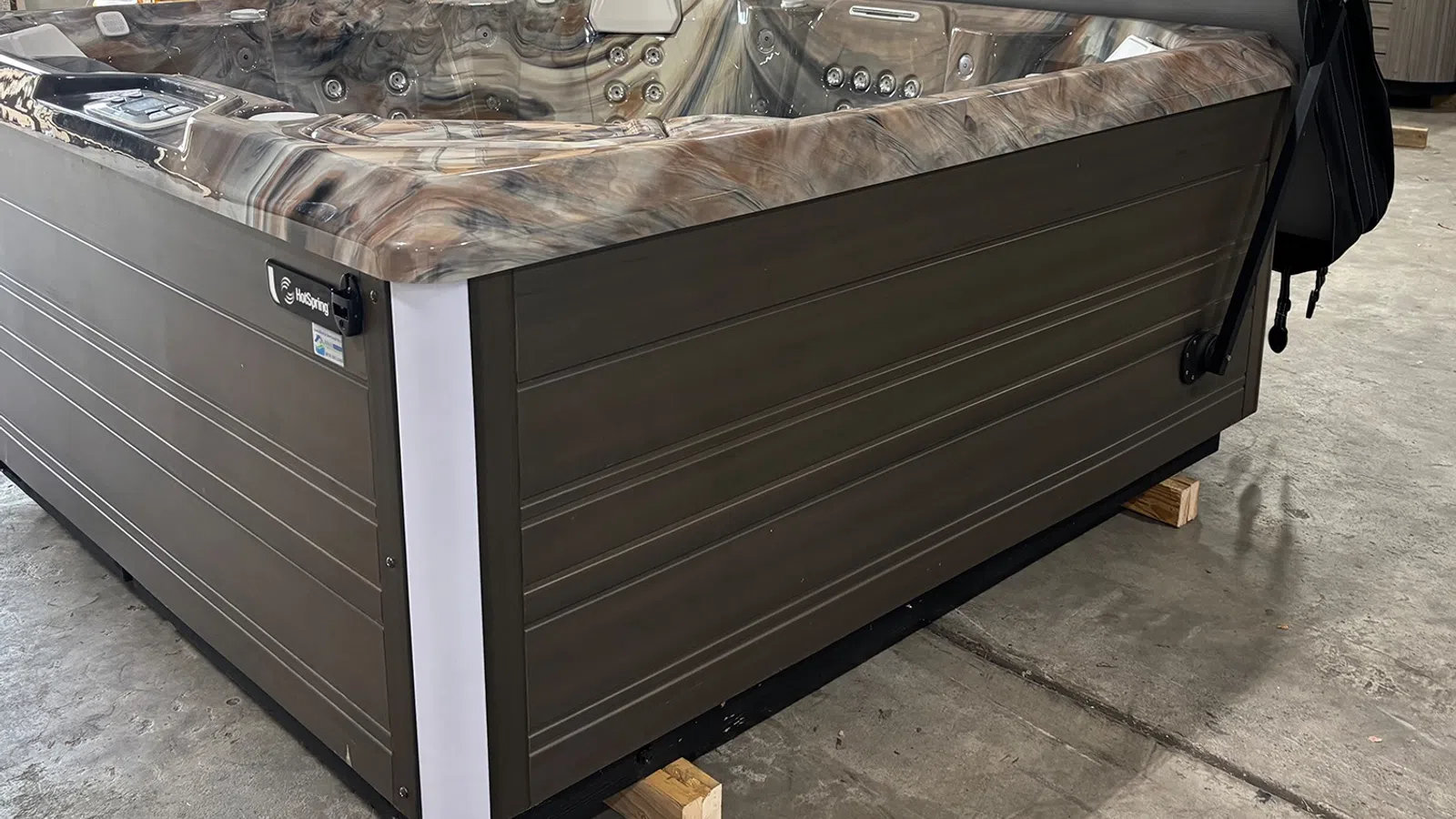 Modern outdoor hot tub with brown wooden panels and marble-patterned interior seating, set on concrete floor.