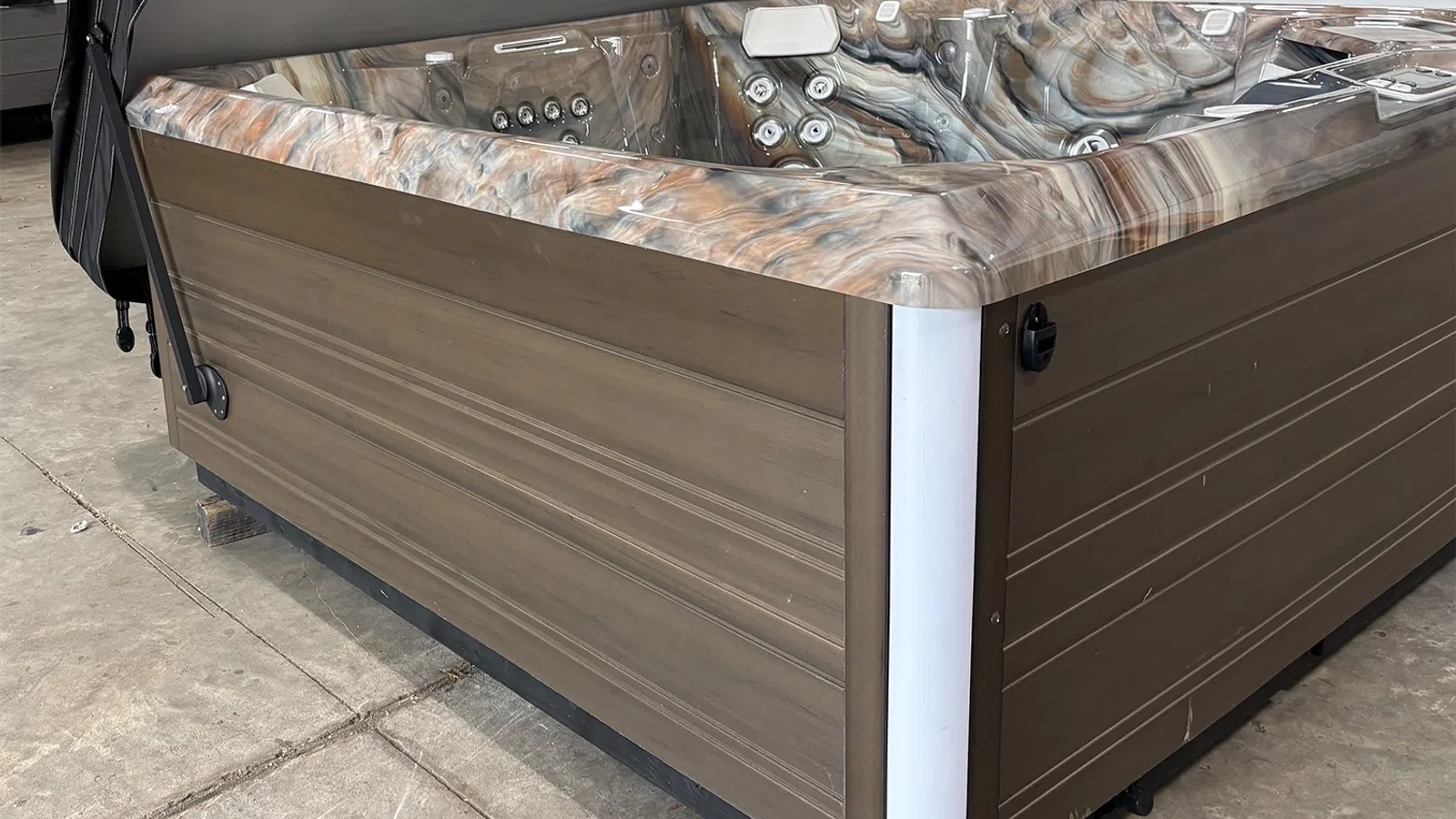 Modern outdoor hot tub with wood paneling and marble-effect interior jets on concrete floor.