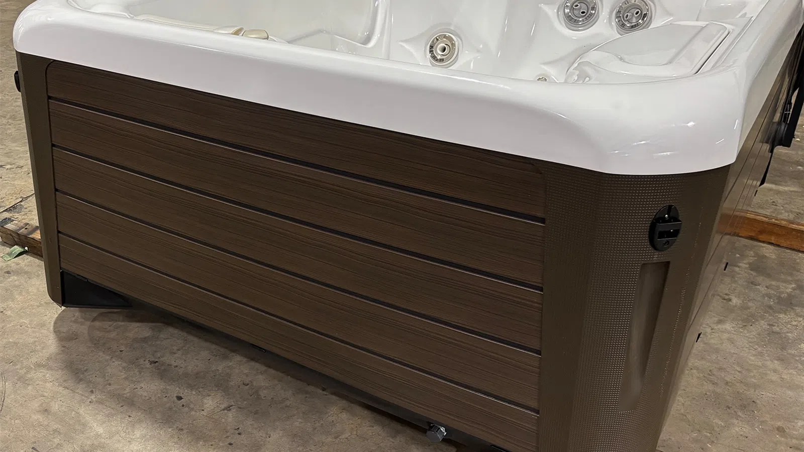 White and brown outdoor hot tub with jets and wood paneling, set on a concrete floor indoors.