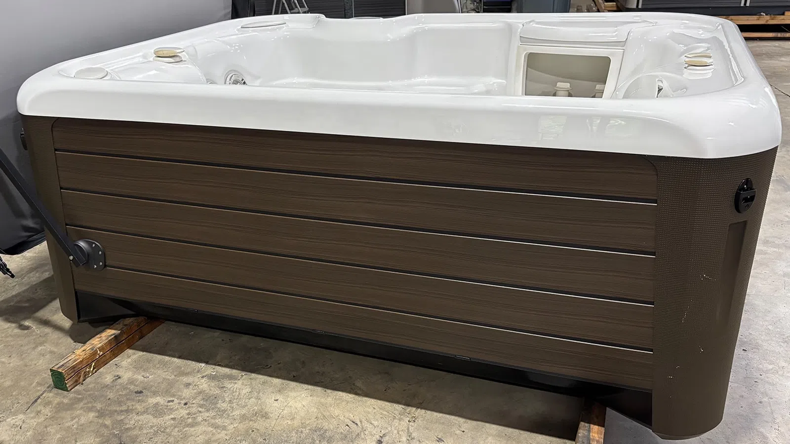 White and brown modern hot tub with seating and control panel, placed indoors on wooden supports