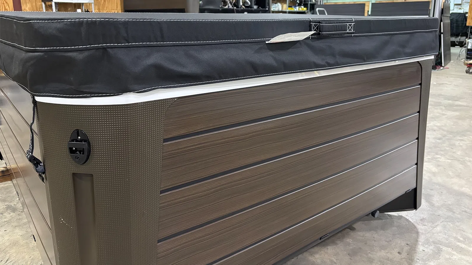 Close-up of a modern hot tub with wood paneling and a black insulated cover in a showroom.